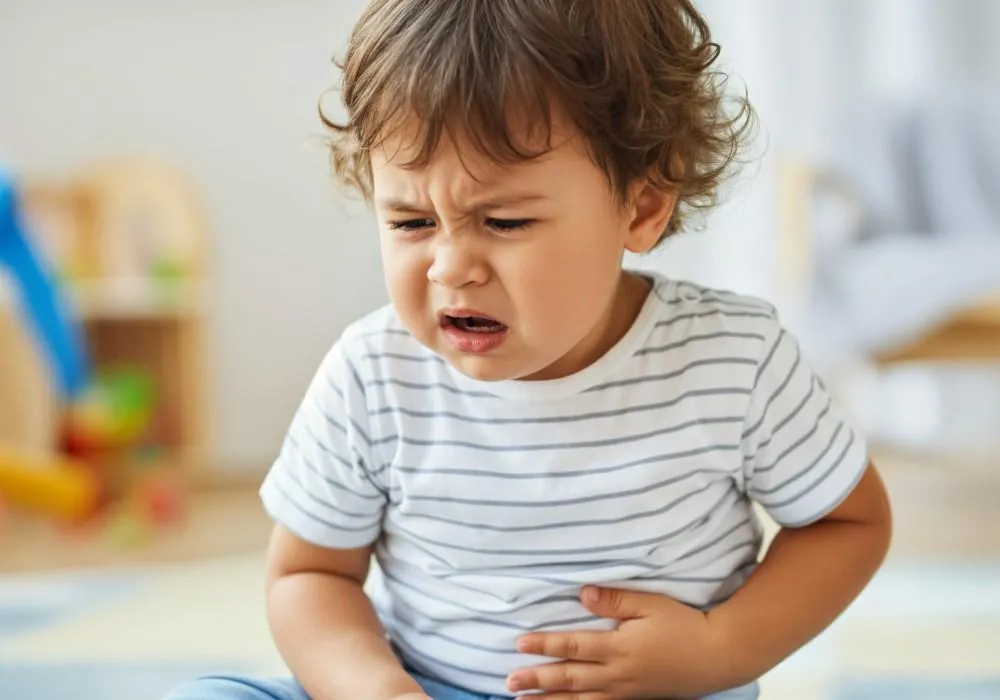 A toddler in a striped shirt grimaces and holds their stomach.