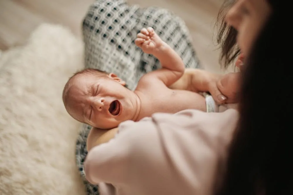 A mother holds her crying newborn close during a feeding attempt.