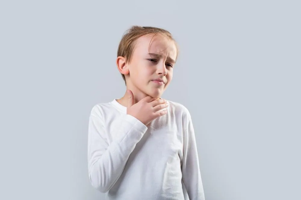 A child in a white shirt winces and holds a hand to their throat.