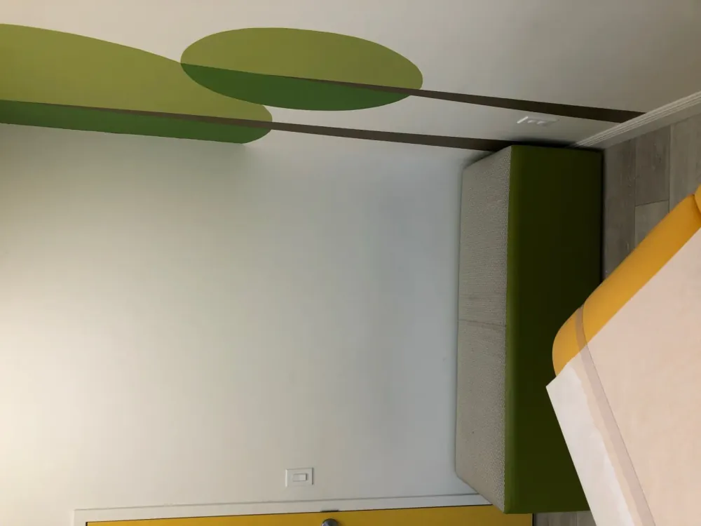 Corner of an exam room with a green bench seat beside a painted tree mural.