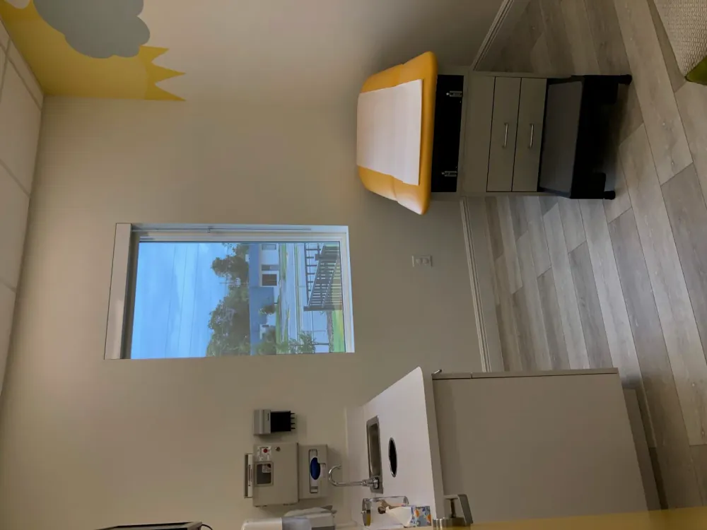 Exam room with a window overlooking the street and a sun-and-clouds mural above the exam table.