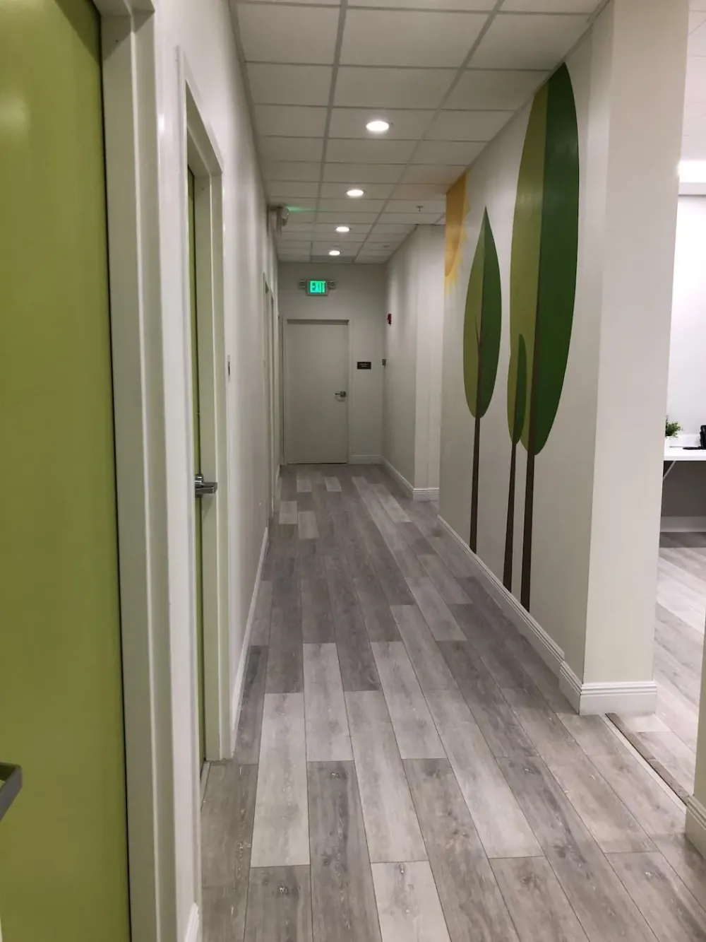 Corridor with green doors and a painted tree mural leading toward the reception area.