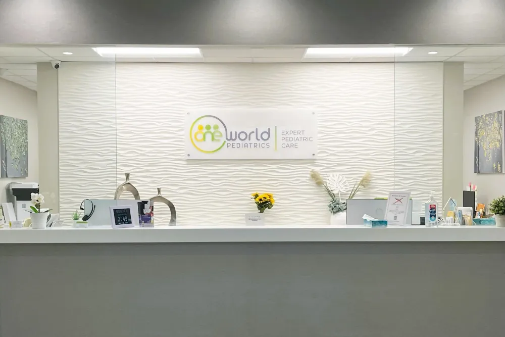 Front desk with the One World Pediatrics sign mounted on the wave-panel wall behind it.