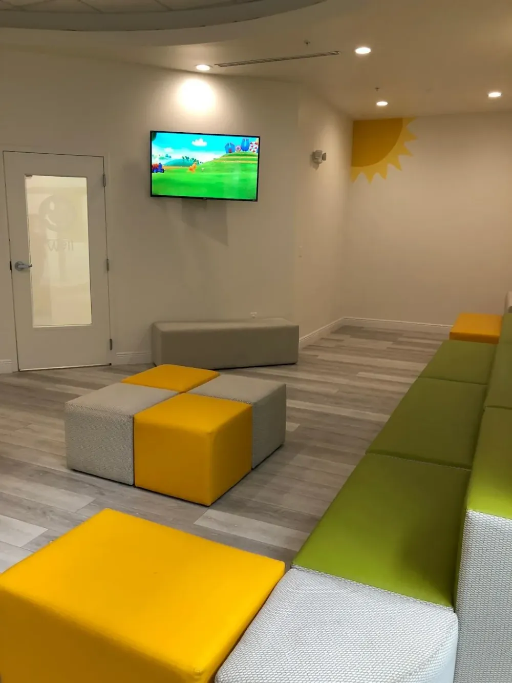 Waiting area with cube seating and a wall-mounted television playing a children’s cartoon.