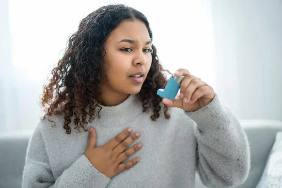 A child holding an asthma inhaler with a spacer up to their mouth.