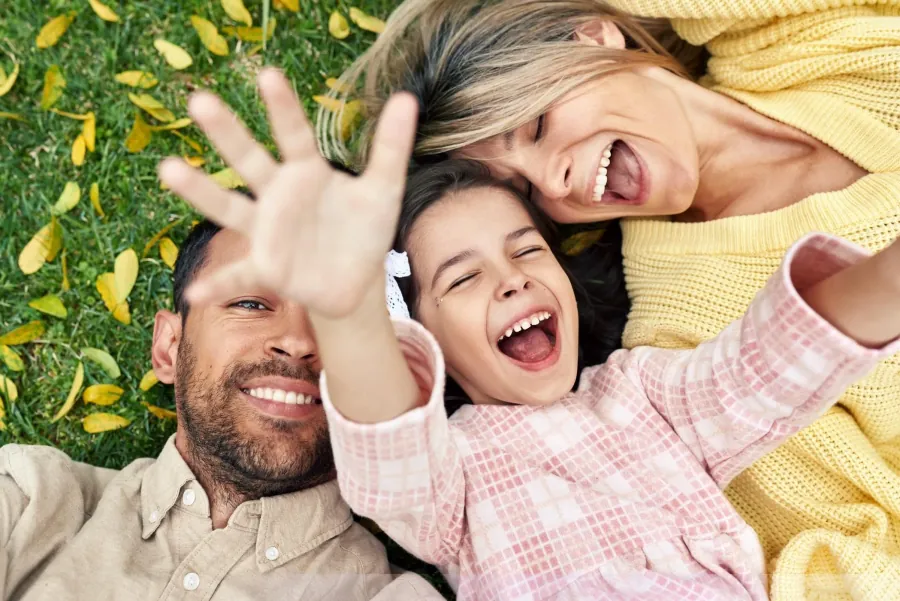 A mother, father and young daughter lying on the grass together, laughing, photographed from above.