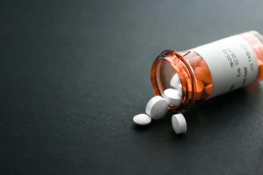 An open prescription bottle on a dark surface with white tablets spilling out beside it.